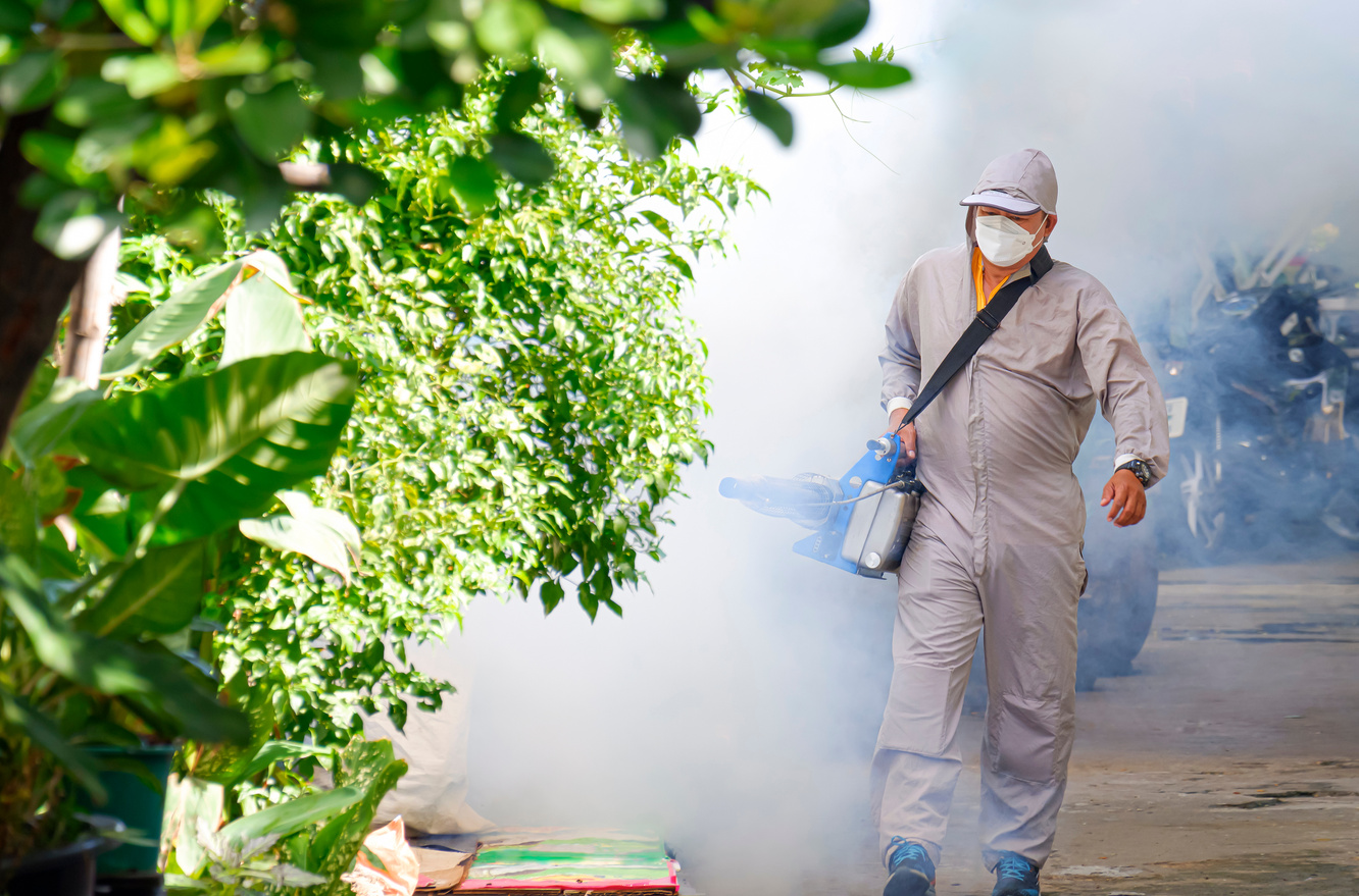 Outdoor healthcare worker using fogging machine spraying chemical to eliminate mosquitoes and prevent dengue fever in slum area